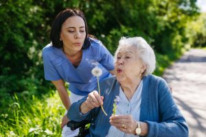 Female,Caregiver,And,Senior,Woman,In,Wheelchair,Holding,Dandelion,,Picking