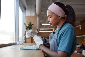 Side view portrait of young African-American woman cleaning windows with sanitizer in cafe, copy space