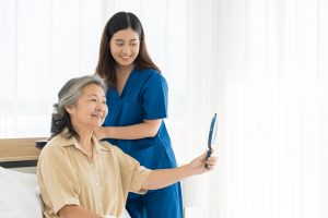 Caregiver, nurse assistant, senior concept. A woman in a blue uniform is helping an older woman with her hair.
