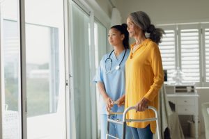 Side view of healthcare worker and woman using walking aid indoor. Authentic Senior Retired Life Concept